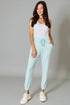 Woman wearing light blue jogger pants and a white top on a gray background