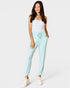 Woman wearing light blue jogger pants and a white tank top on a white background