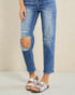 Person wearing ripped blue jeans and silver sandals on a beige background