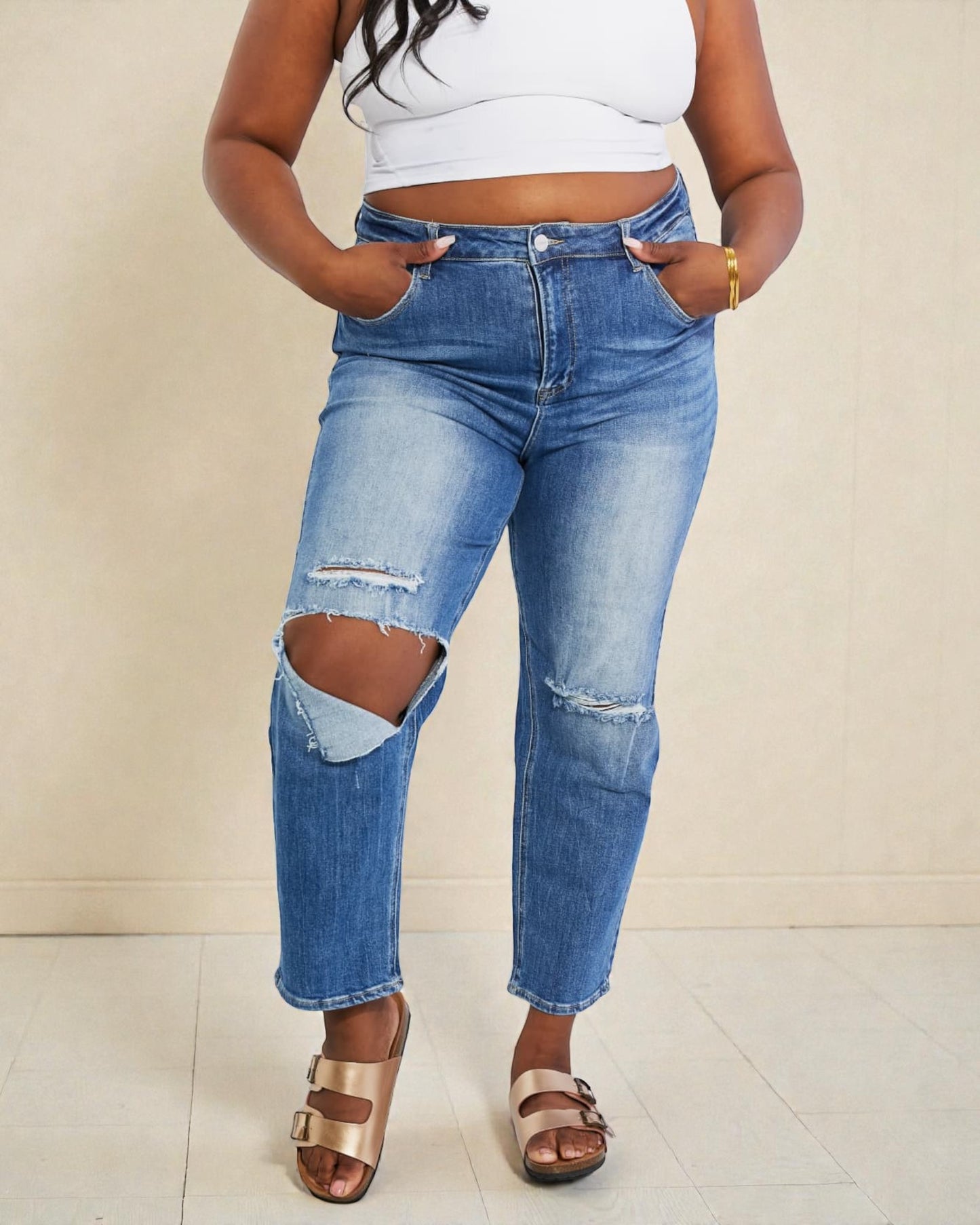 Person wearing ripped blue jeans and a white top against a beige background