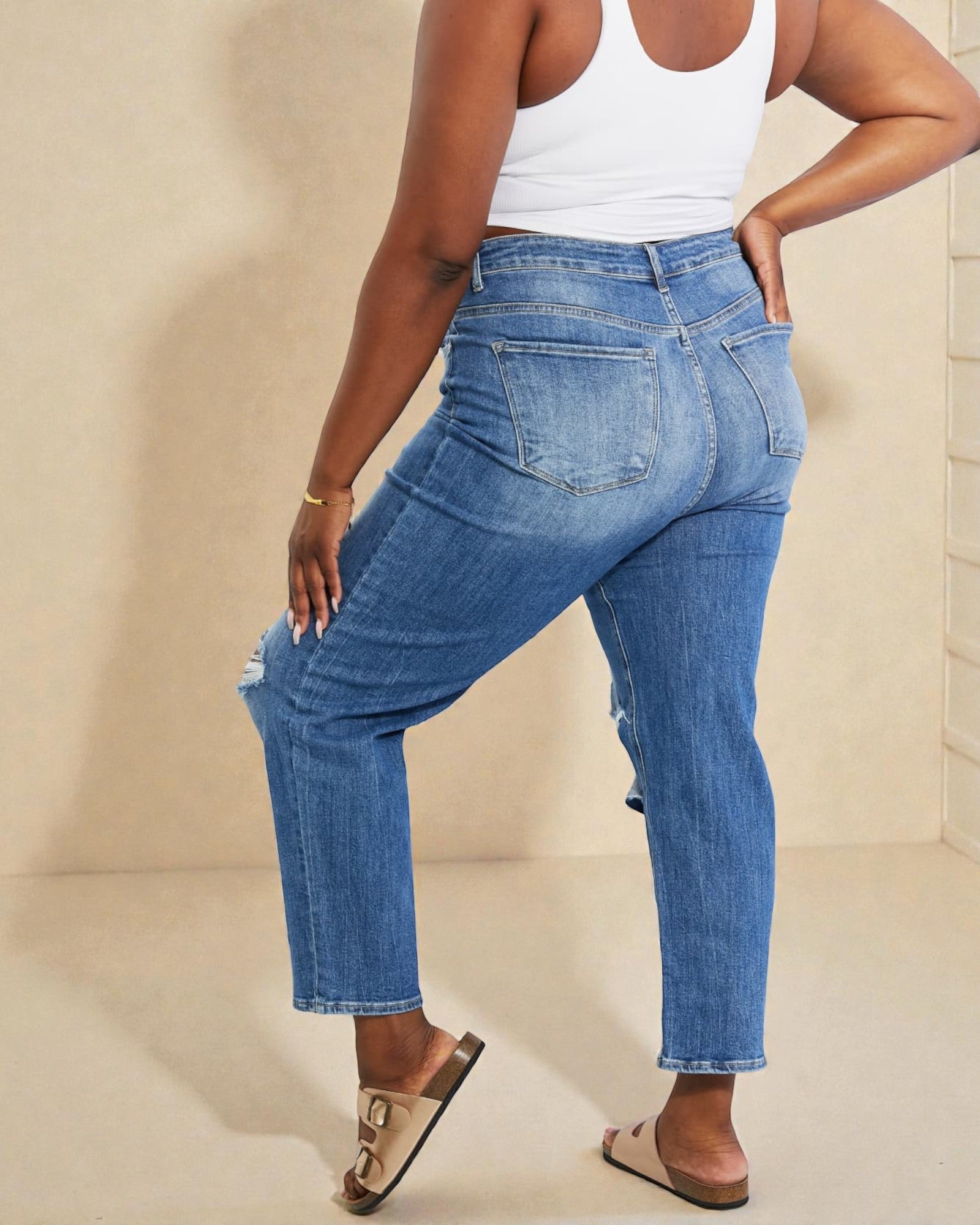 Person wearing blue jeans and a white tank top on a beige background