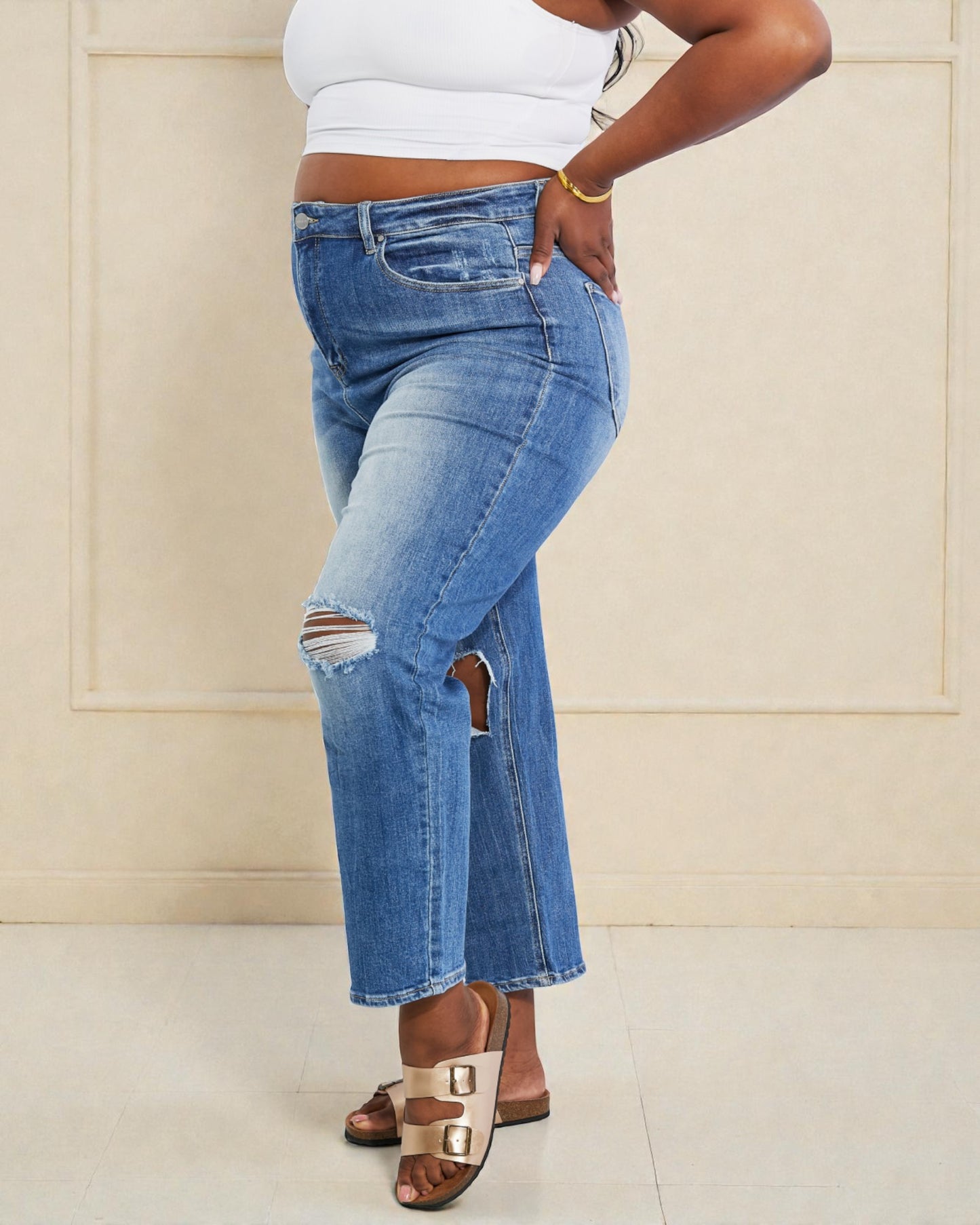 Person wearing ripped blue jeans and a white top against a beige wall.