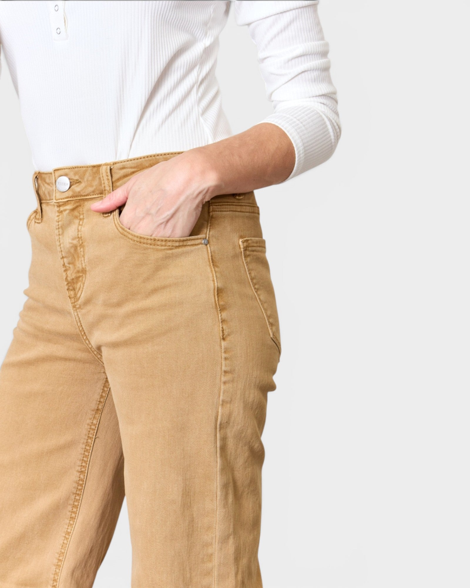 Person wearing beige pants with a white shirt on a plain background