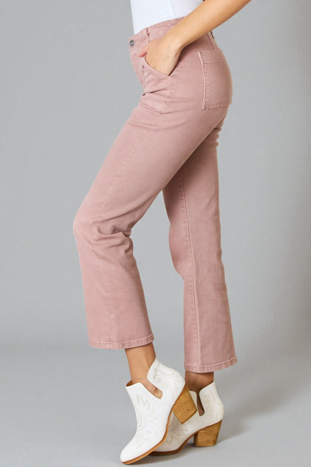 Person wearing pink jeans and white ankle boots on a gray background