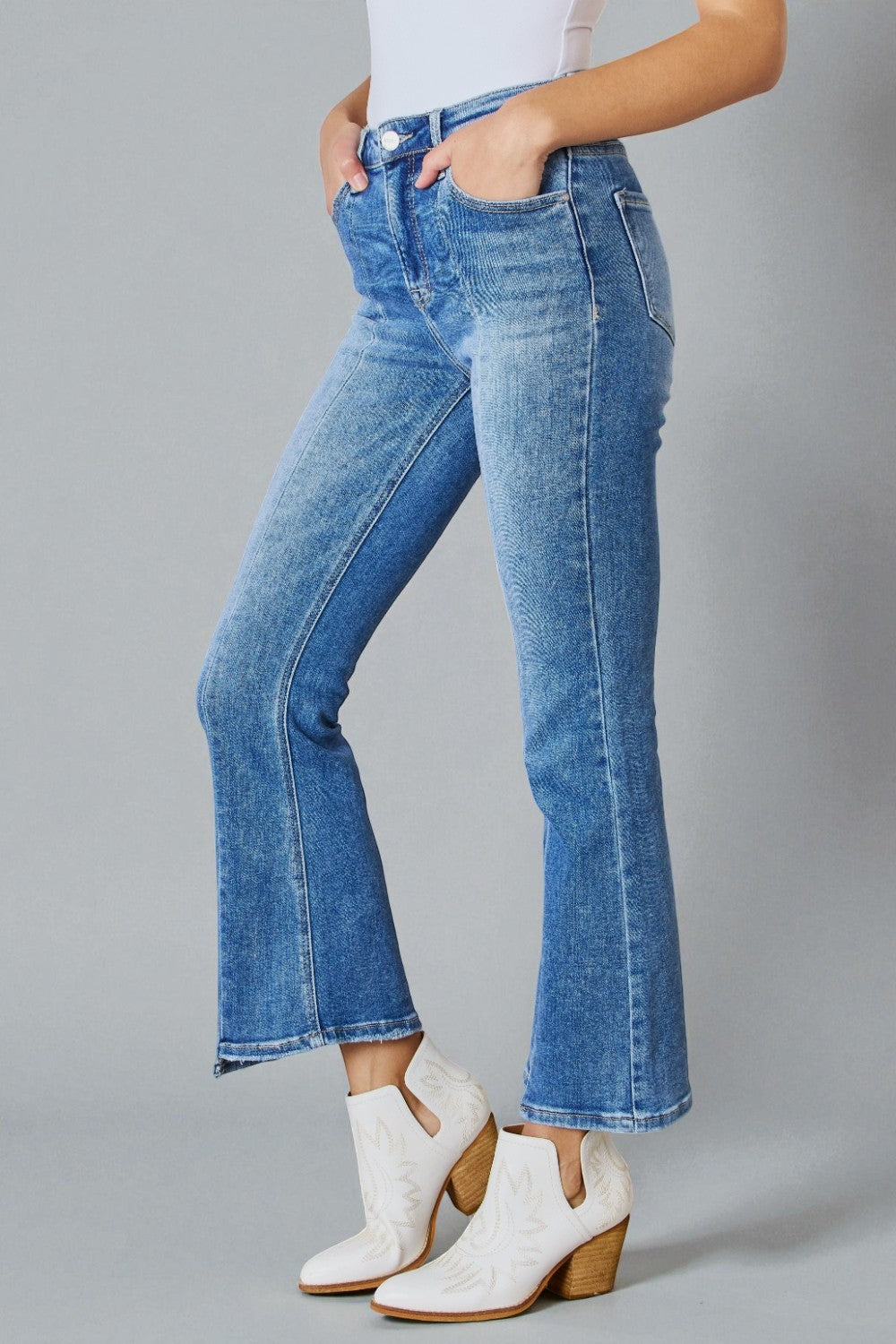 Person wearing blue jeans and white boots on a gray background