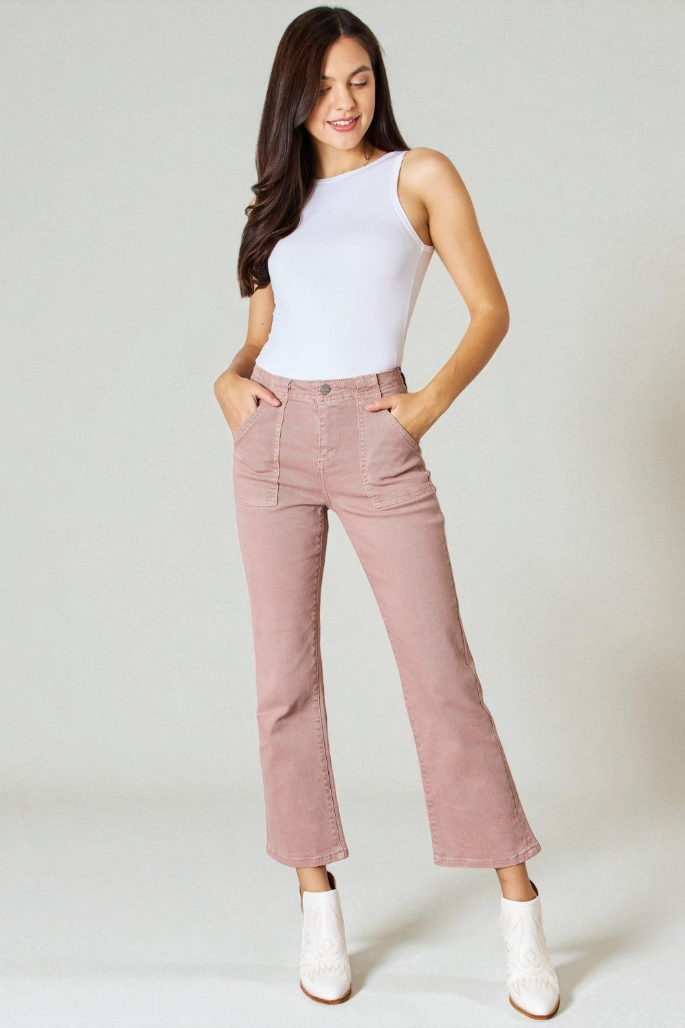 Woman wearing a white sleeveless top and pink pants on a plain background