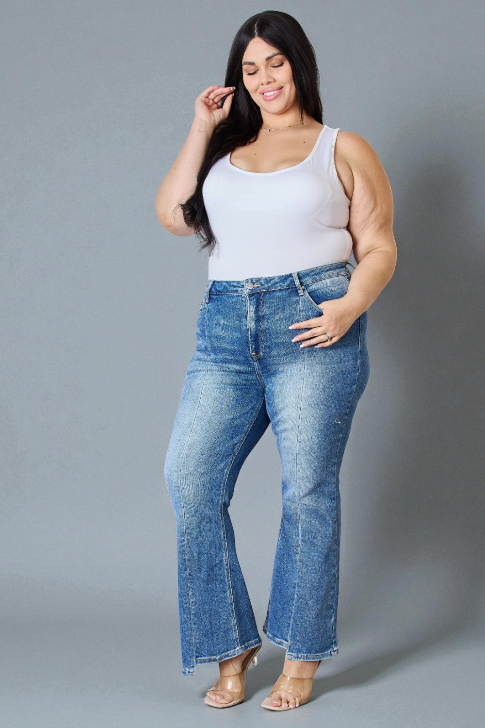 Woman wearing blue jeans and a white tank top against a gray background