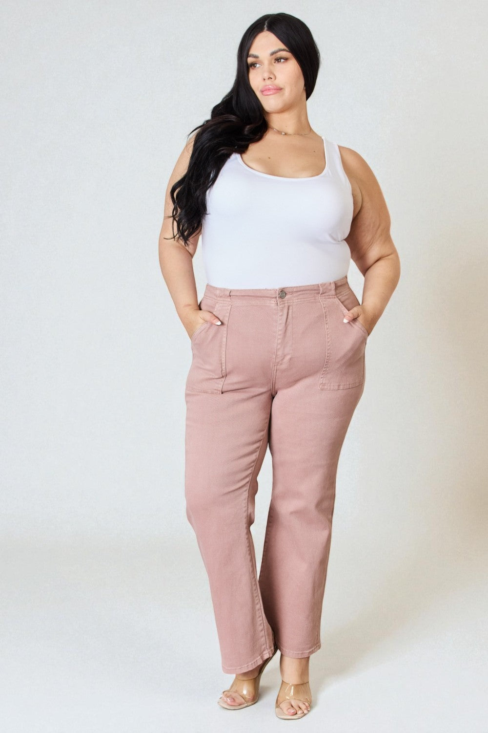 Woman wearing a white tank top and pink pants on a plain background