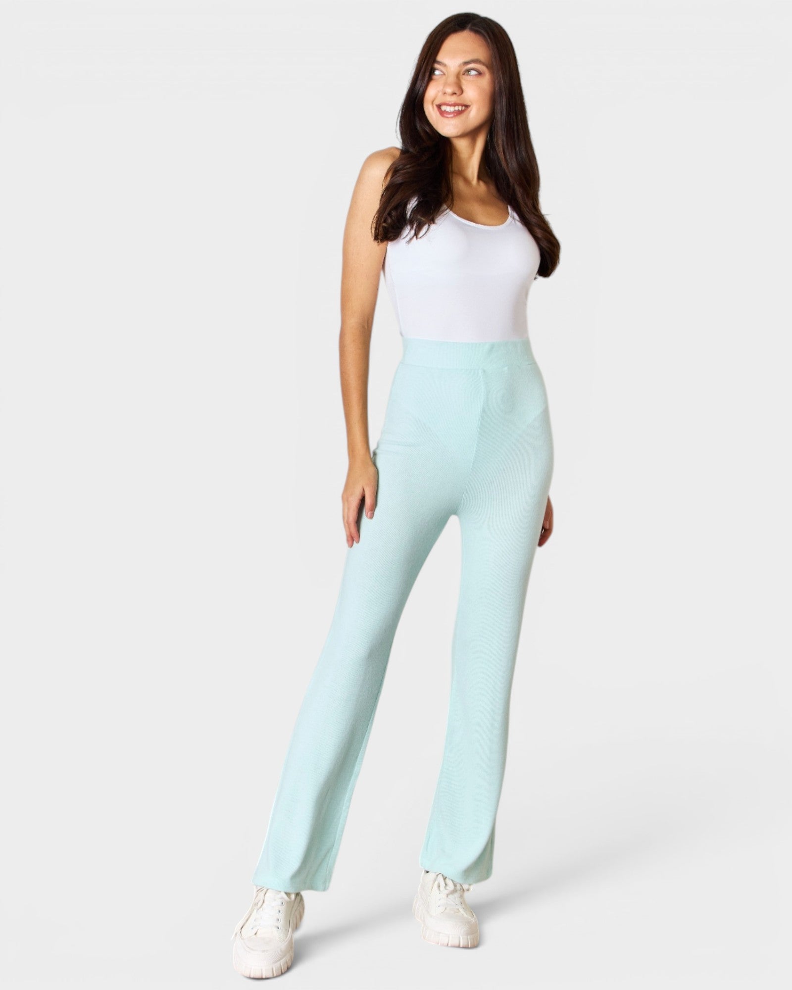 Woman wearing light blue pants and a white top on a white background
