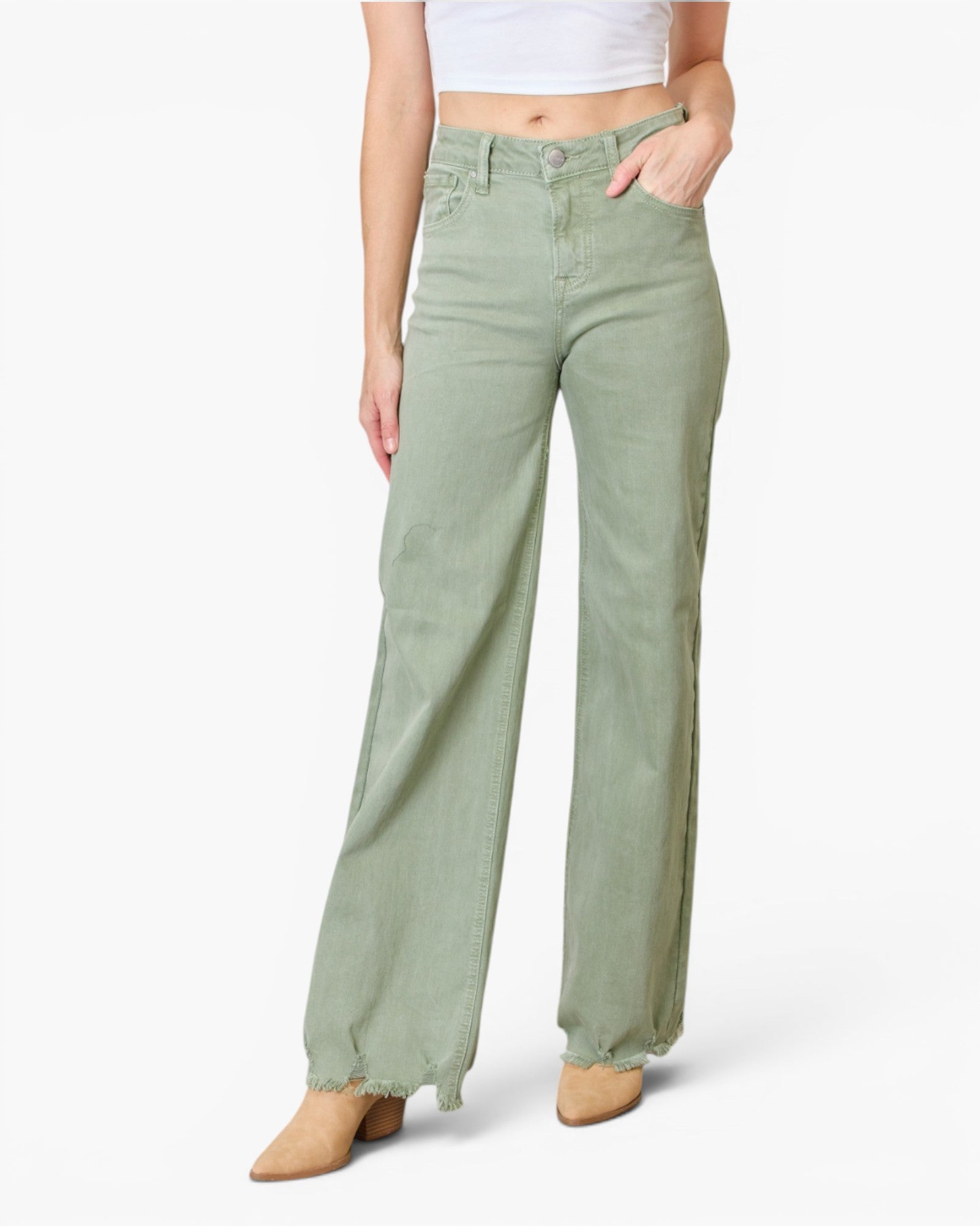 A model wearing sage green wide-leg jeans with raw, frayed hems, paired with a white crop top and tan pointed-toe heels, against a plain white studio background.