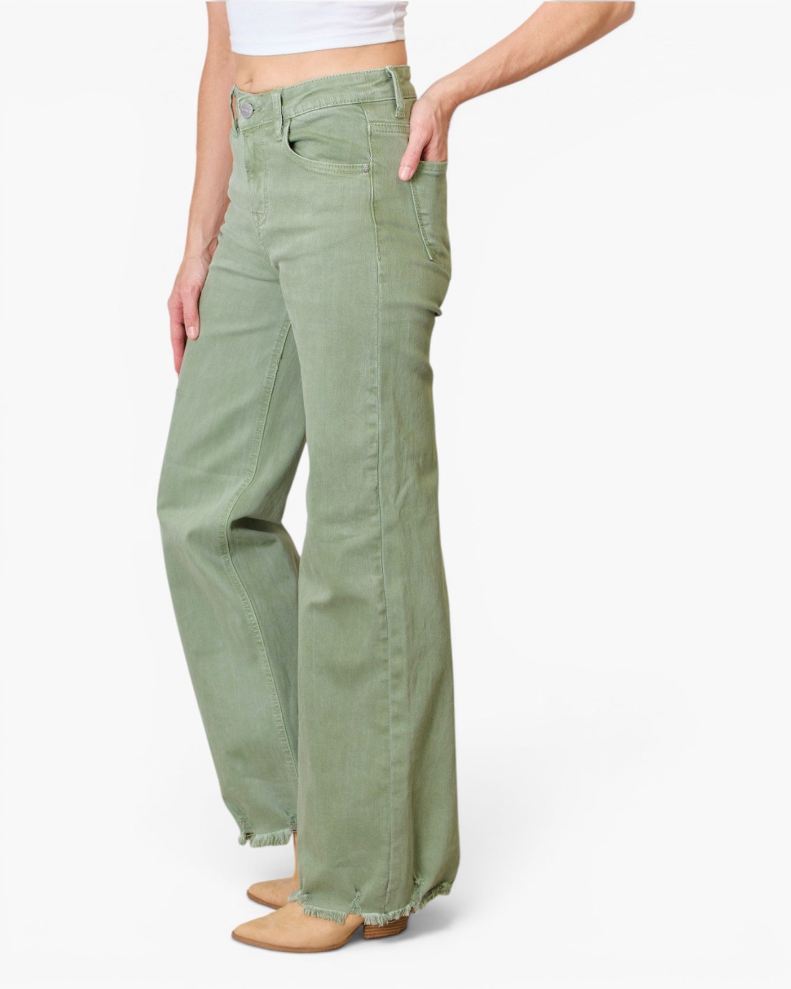 A model wearing sage green wide-leg jeans with a frayed hem, paired with a white crop top and tan boots, shown from the waist down on a white studio background.