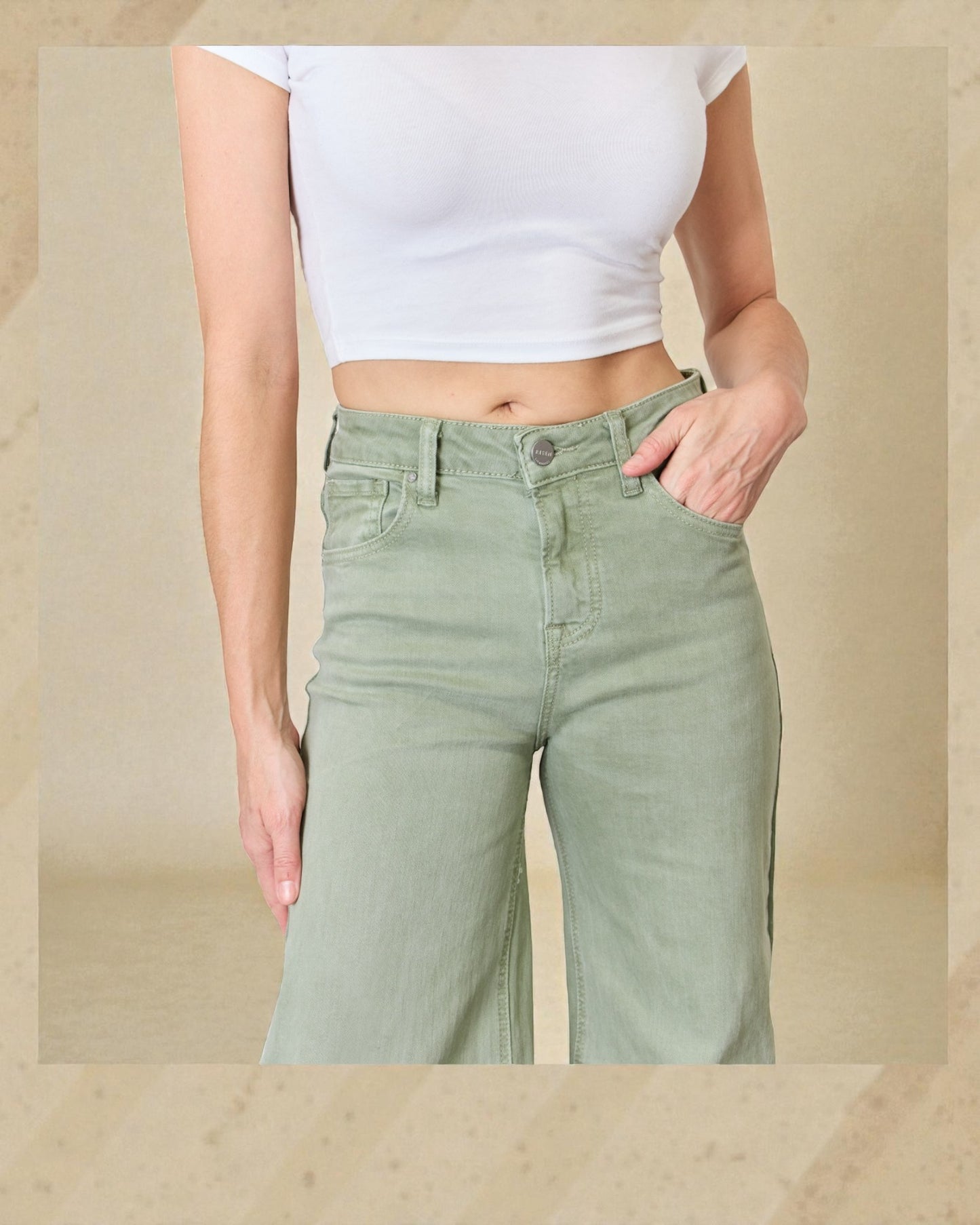 Person wearing light green pants and a white crop top on a beige background