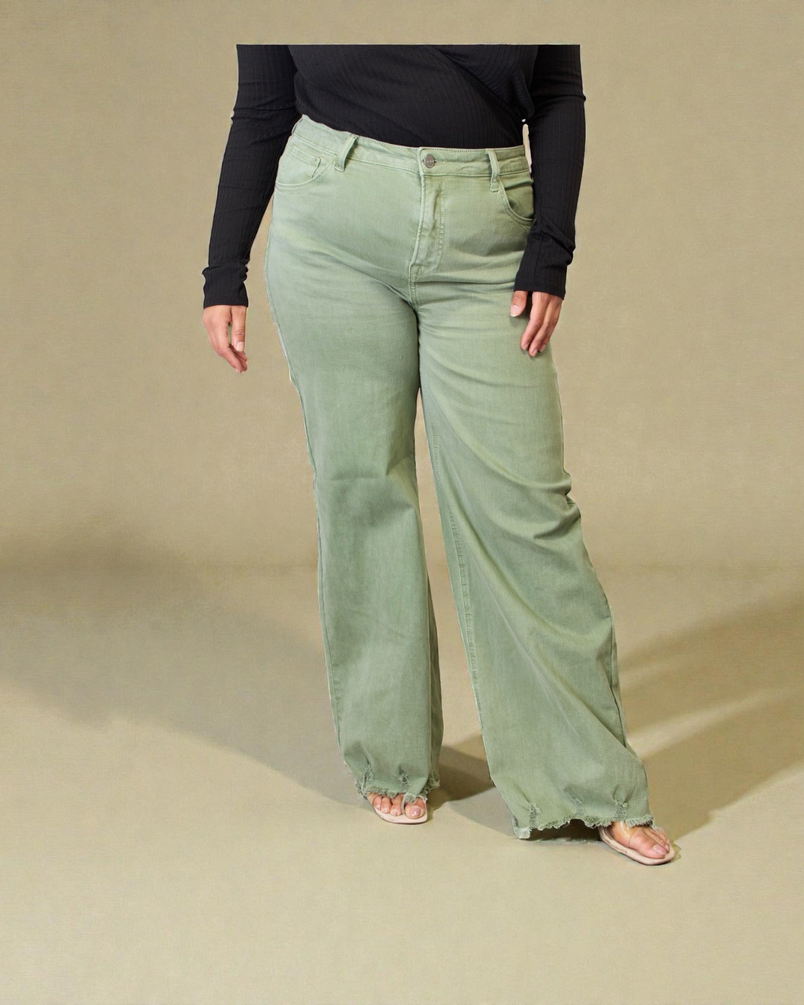 Person wearing light green pants and a black top on a beige background