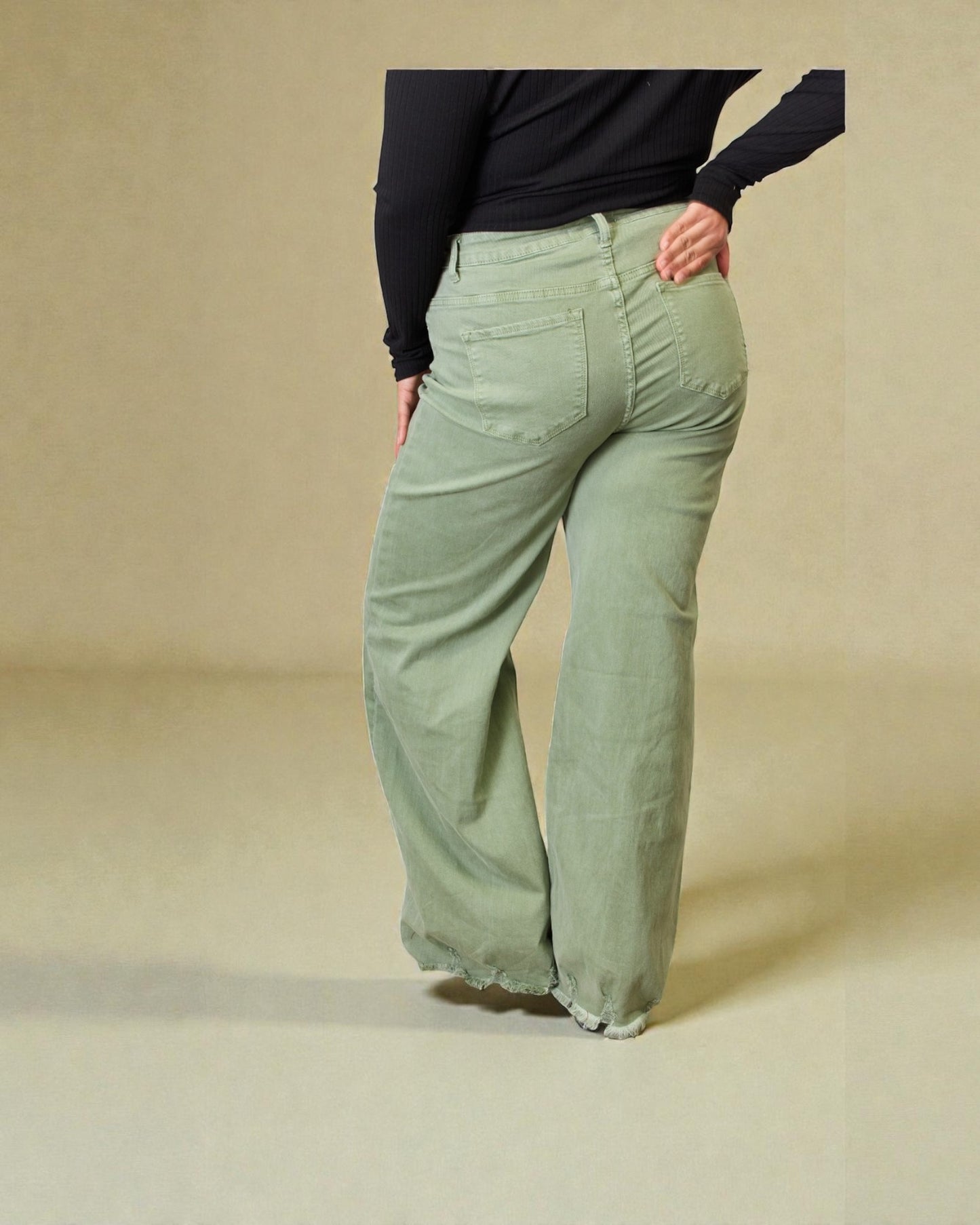 Person wearing light green pants and a black top on a beige background