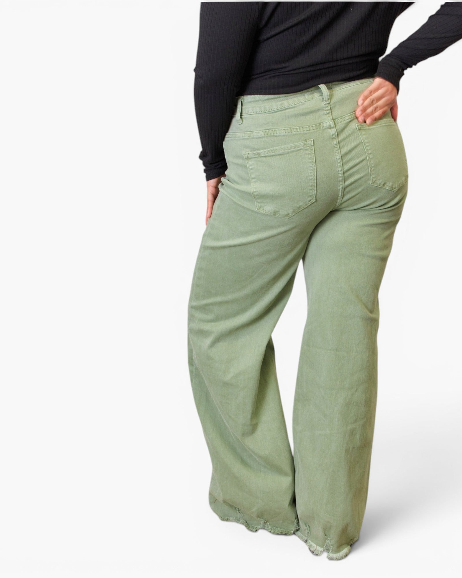 A person shown from the back wearing light sage green wide-leg pants and a black long-sleeve top against a plain light gray studio background.