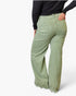 A person shown from the back wearing light sage green wide-leg pants and a black long-sleeve top against a plain light gray studio background.