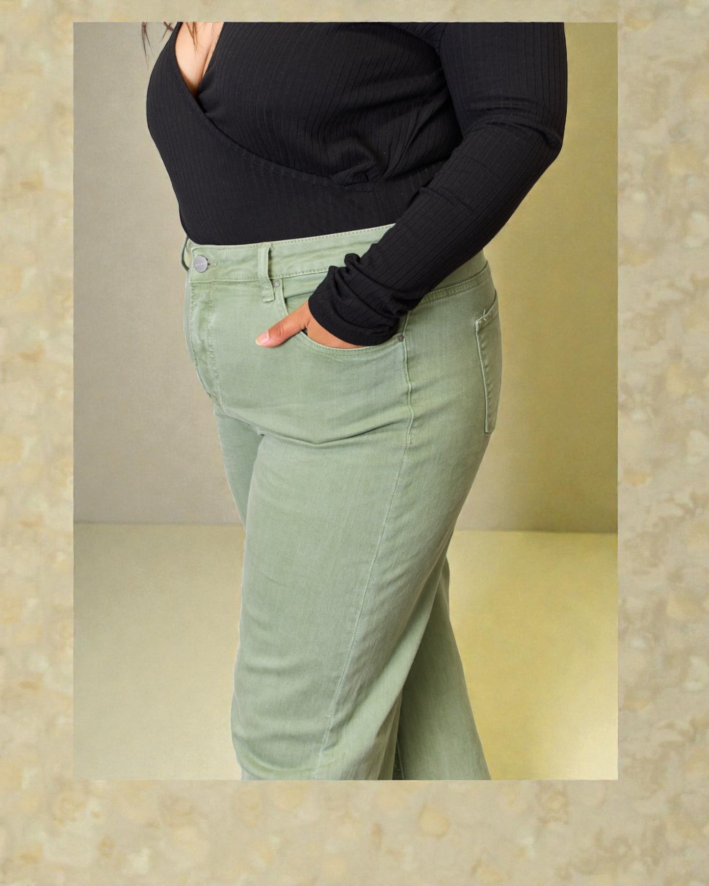 Person wearing a black long-sleeve top and light green pants against a beige background