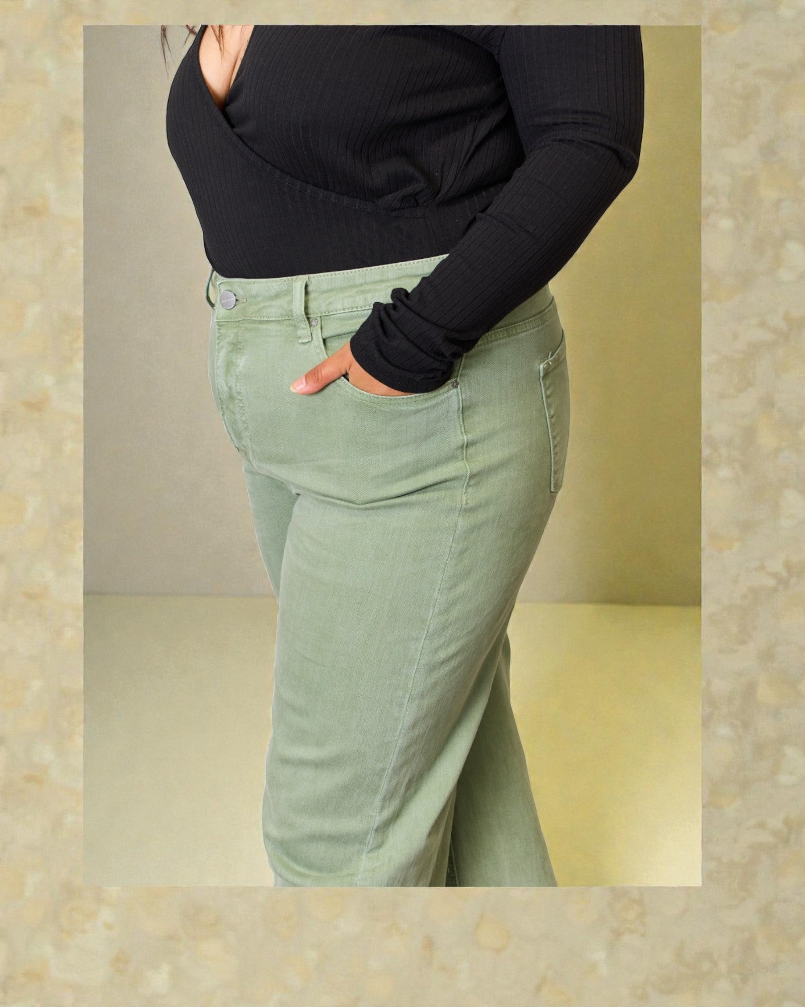 Person wearing a black long-sleeve top and light green pants against a beige background