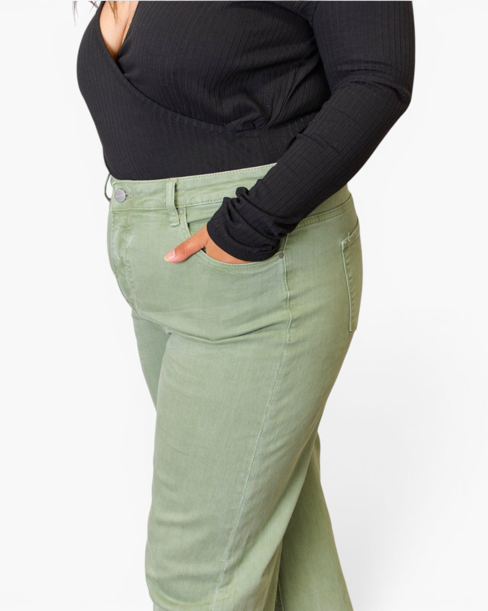A person wearing sage green high-waisted flared jeans and a black ribbed long-sleeve top, shown from the chest down against a plain white background.