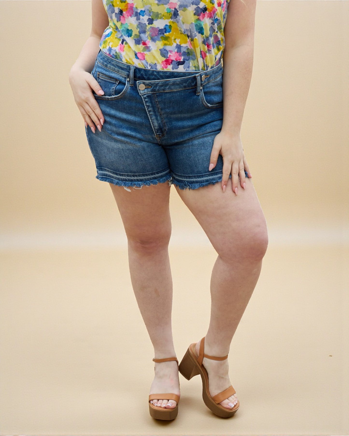 Person wearing a colorful top and denim shorts on a beige background