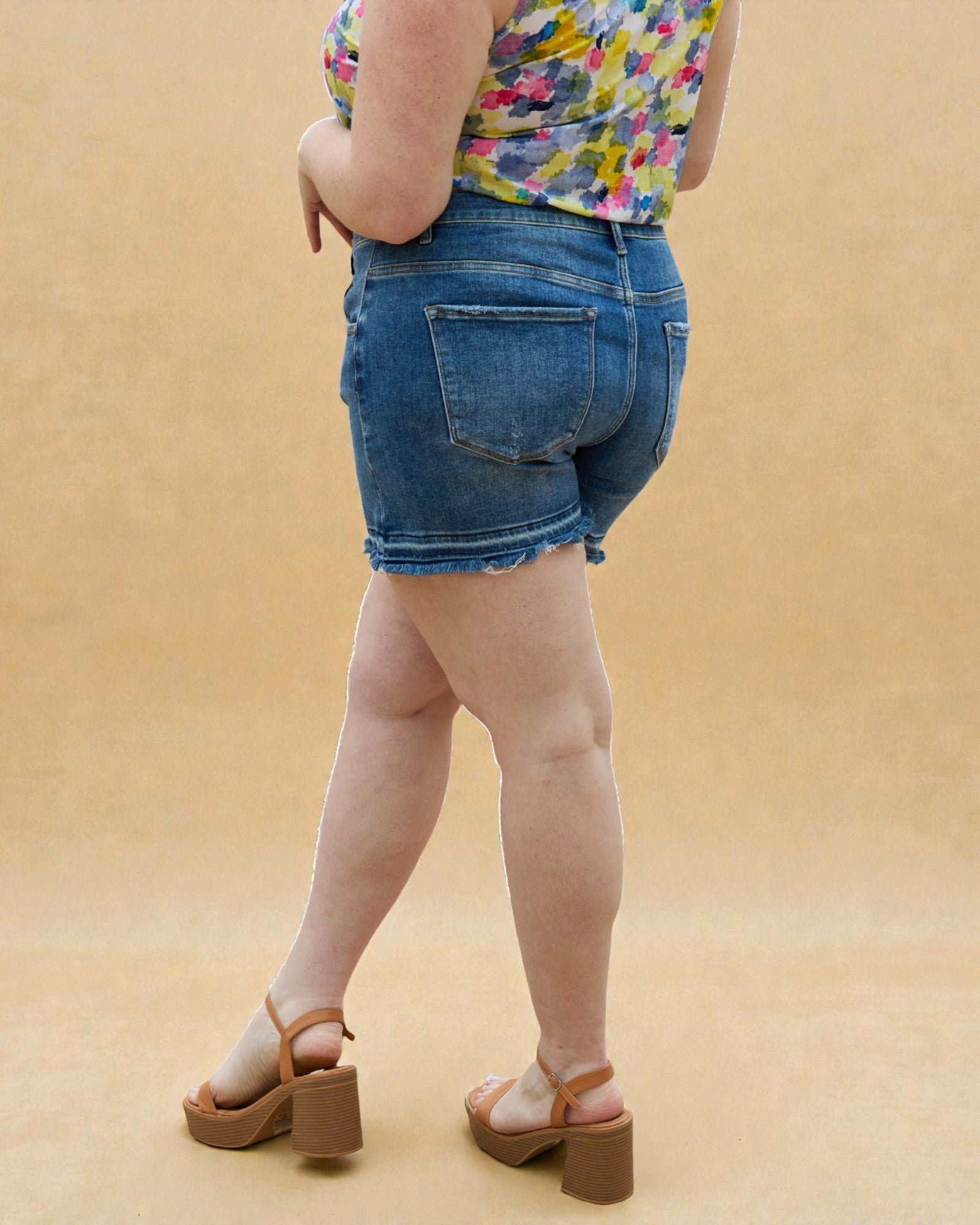 Person wearing denim shorts and a colorful top on a beige background