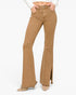 A model wearing tan flare jeans with side slits and frayed hems, paired with a white long-sleeve top and beige pointed-toe heels, against a plain white background.