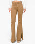 A model wearing tan flare jeans with frayed hems and side slits, paired with a white ribbed long-sleeve top and beige pointed-toe heels, shown against a plain white background.