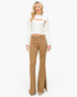 A woman modeling a white long-sleeve knit top with a chest cutout and tan flared jeans against a plain white studio background.