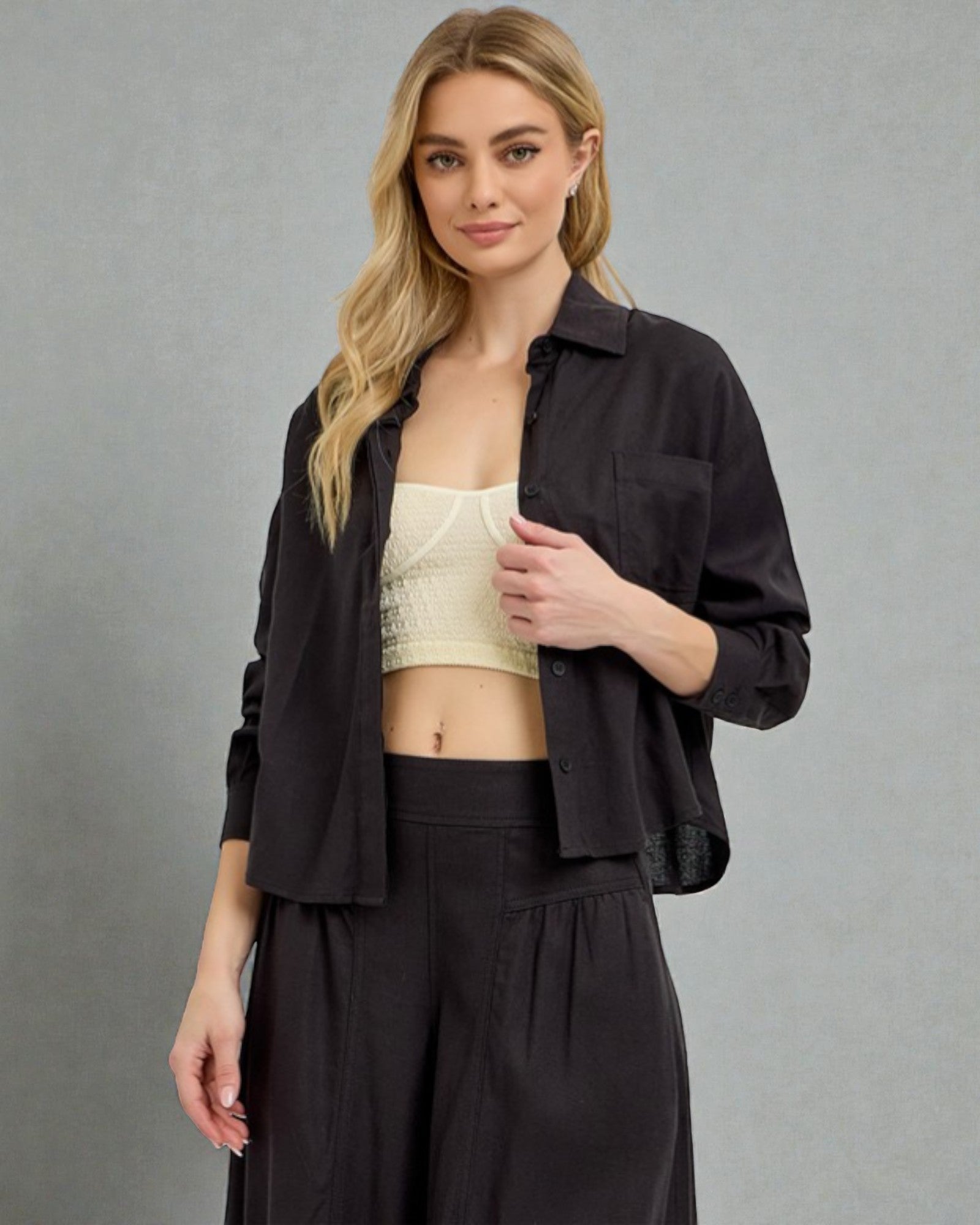 Woman wearing a black shirt over a beige crop top and black pants on a gray background