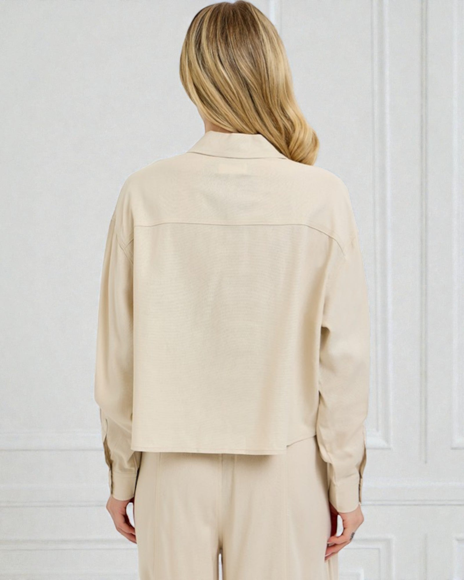 Person wearing a beige jacket and pants against a white wall