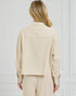 Person wearing a beige jacket and pants against a white wall