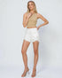 Woman wearing a beige tank top and white shorts on a plain background