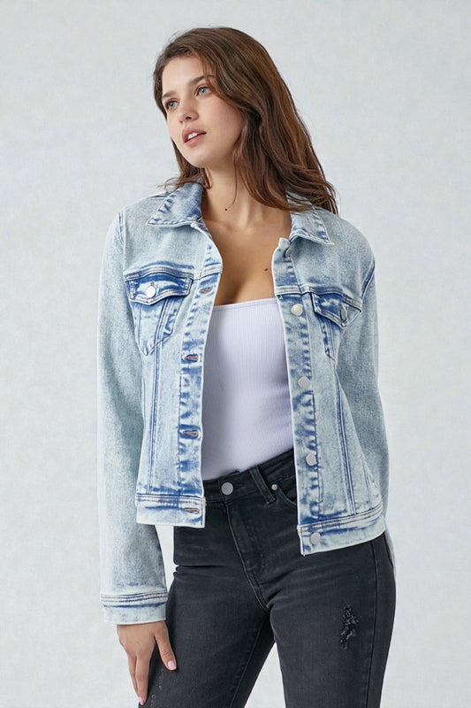 Woman wearing a light blue denim jacket over a white top and black jeans on a plain background