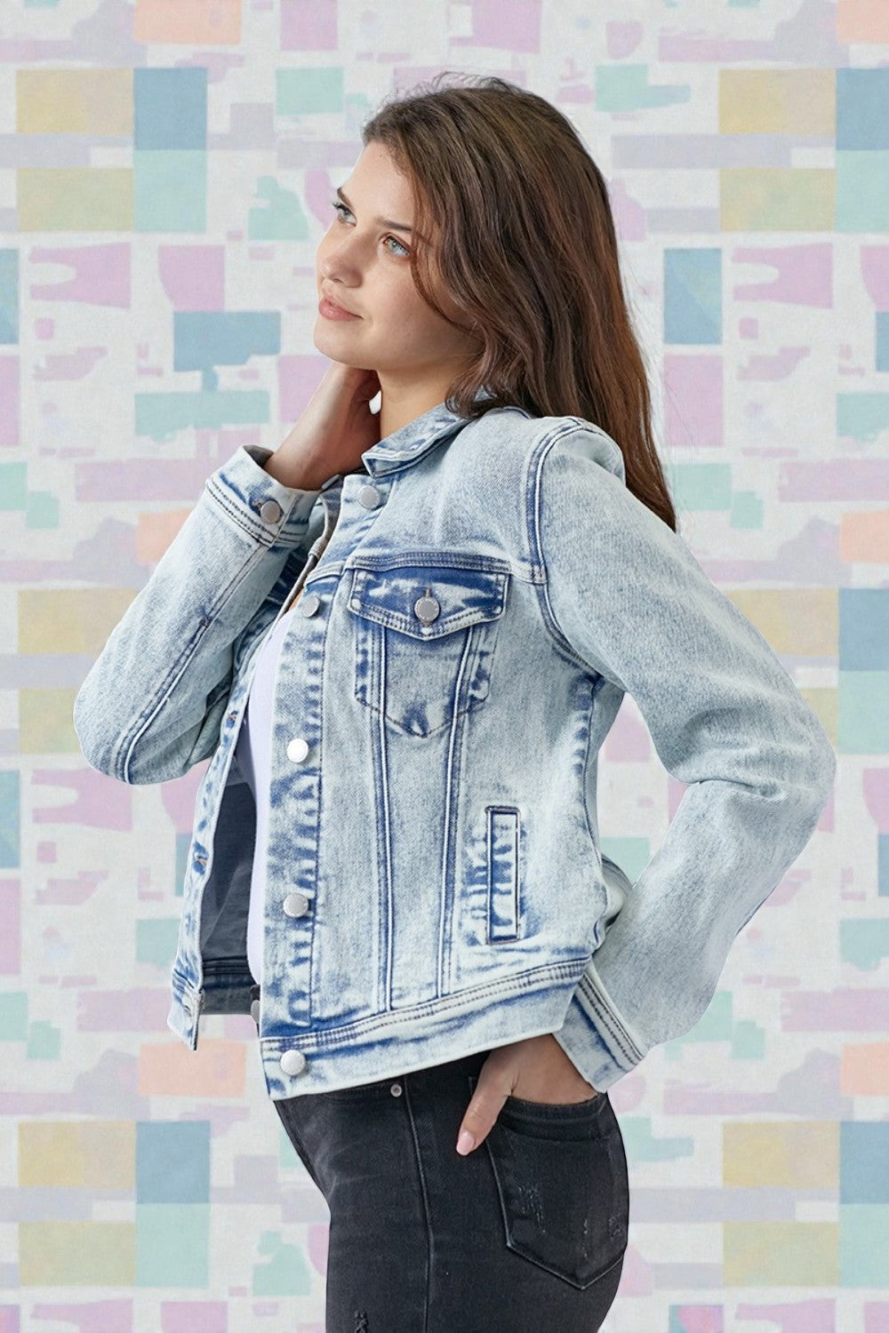 Woman wearing a denim jacket against a colorful geometric-patterned wall.