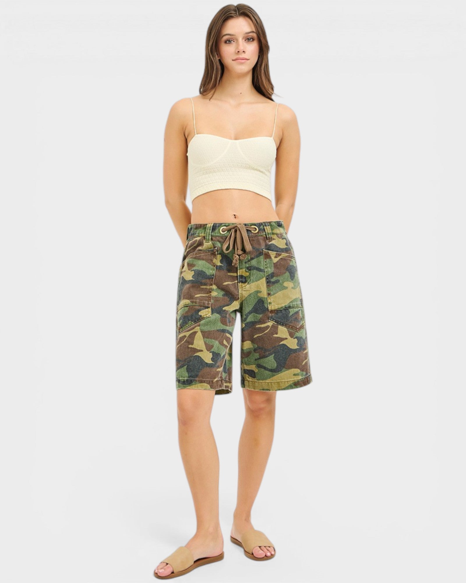 Woman wearing a cream top and camouflage shorts on a white background