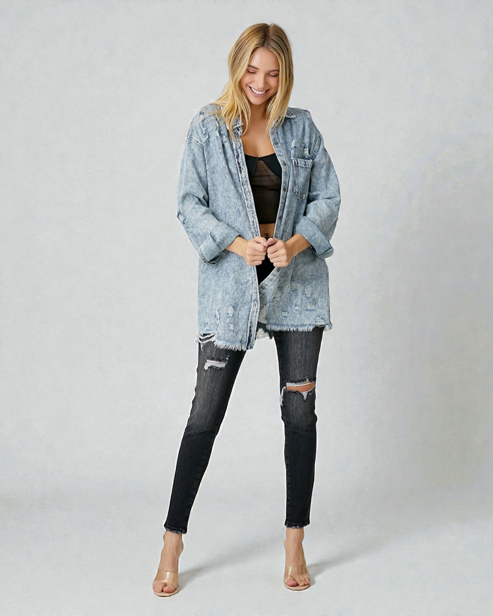 Woman wearing a light blue denim jacket and black ripped jeans on a plain background
