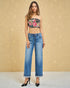 Woman wearing a floral bandeau top and blue jeans against a beige background