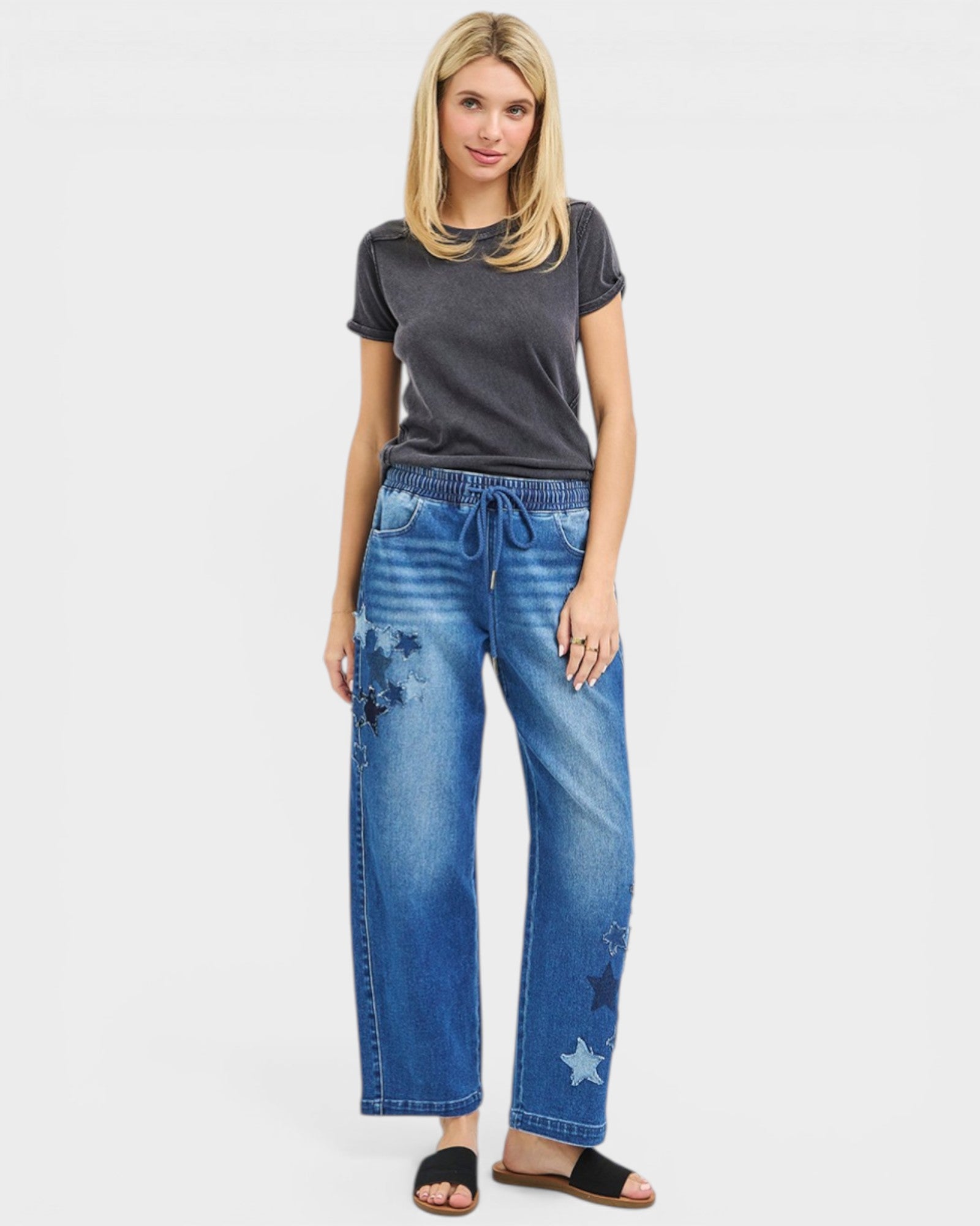 Woman wearing a gray t-shirt and blue jeans with star designs on a white background