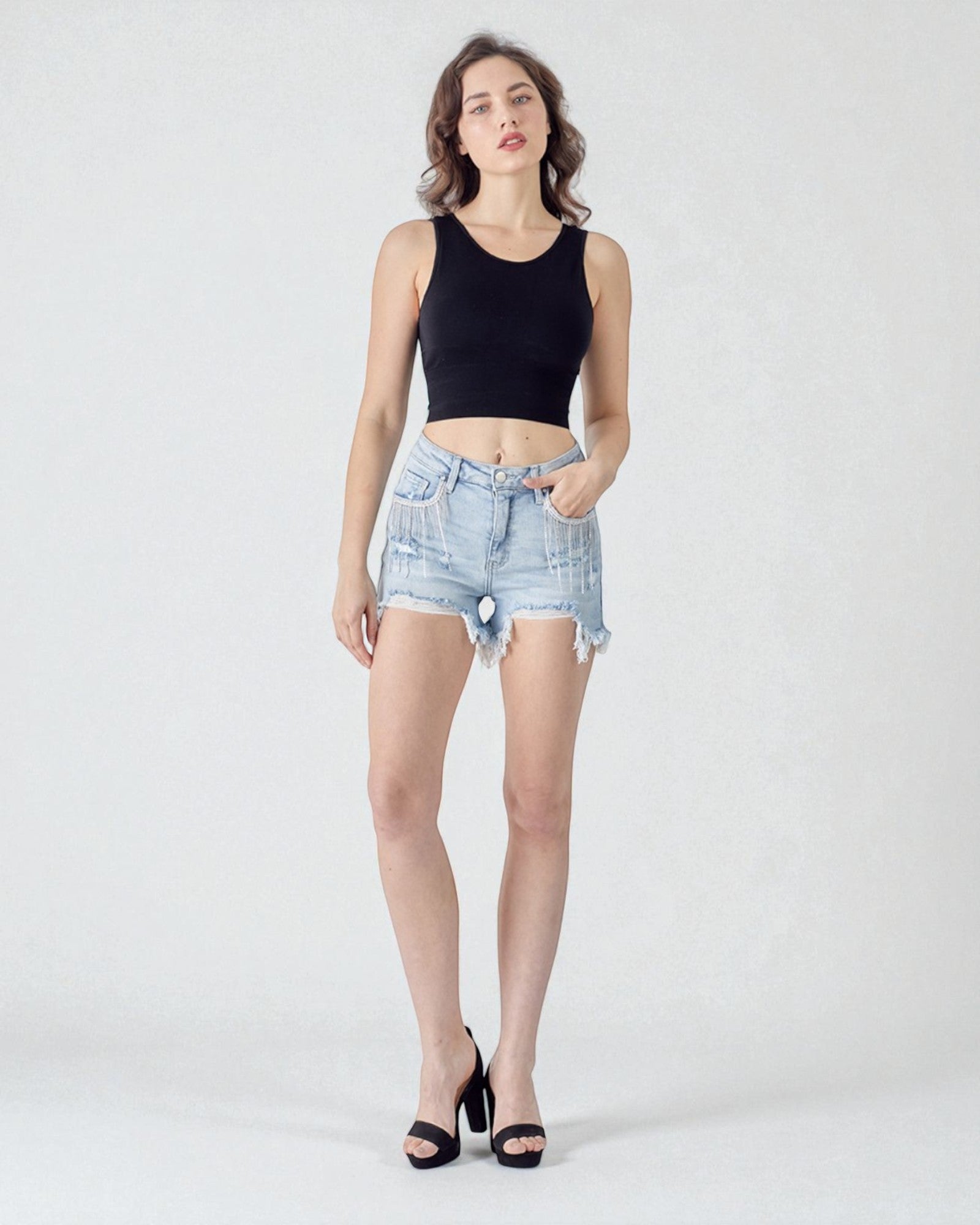Woman wearing a black tank top and light blue denim shorts on a white background