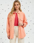 Woman wearing a peach-colored jacket over a pink shirt with a white background