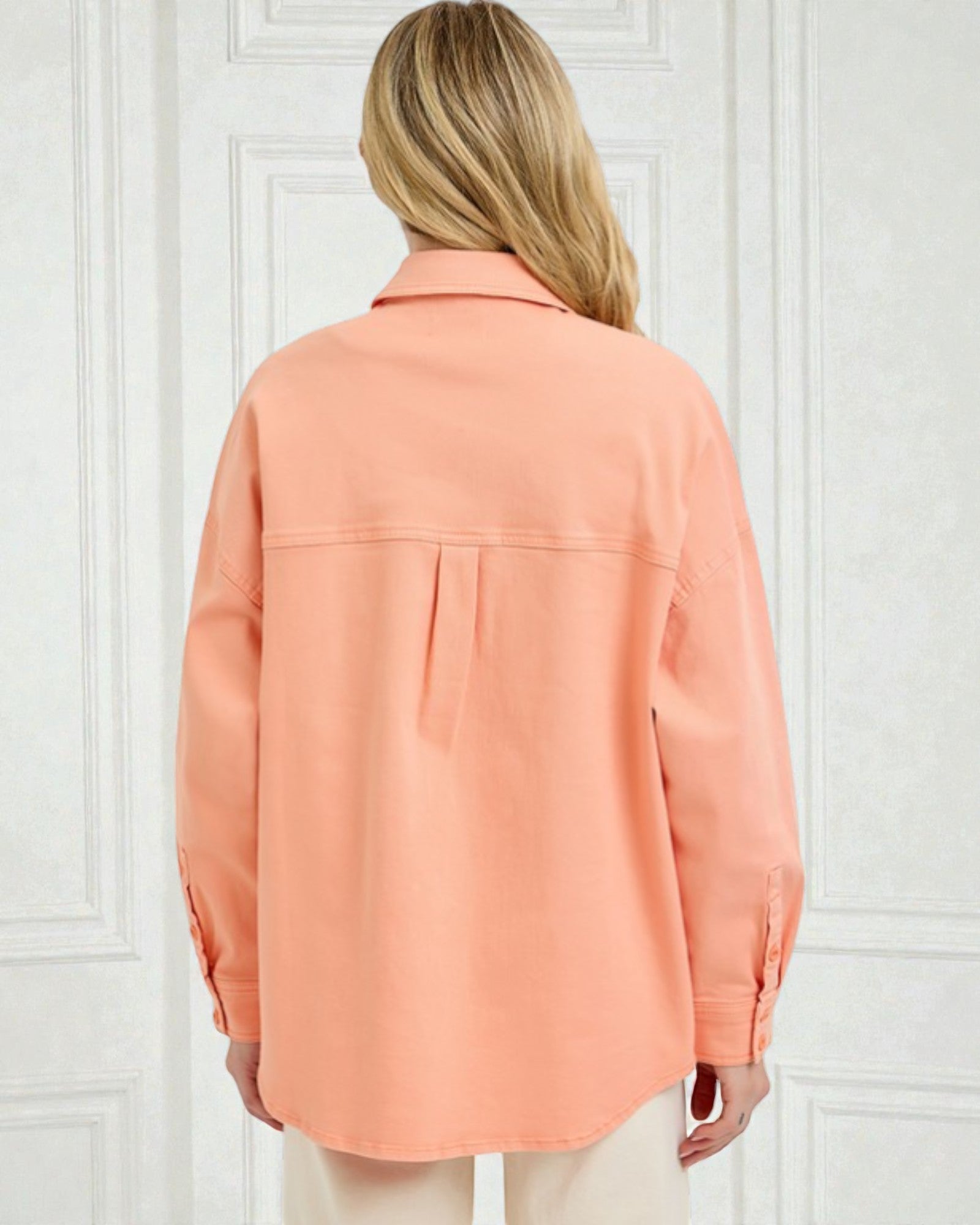 Person wearing a peach-colored shirt against a white paneled wall