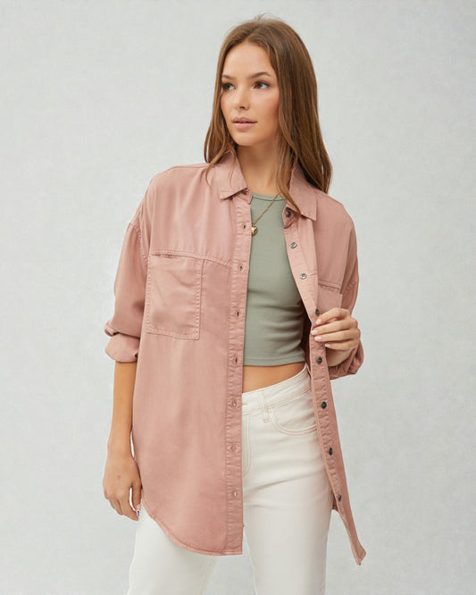 Woman wearing a pink jacket over a green top and white pants on a light gray background