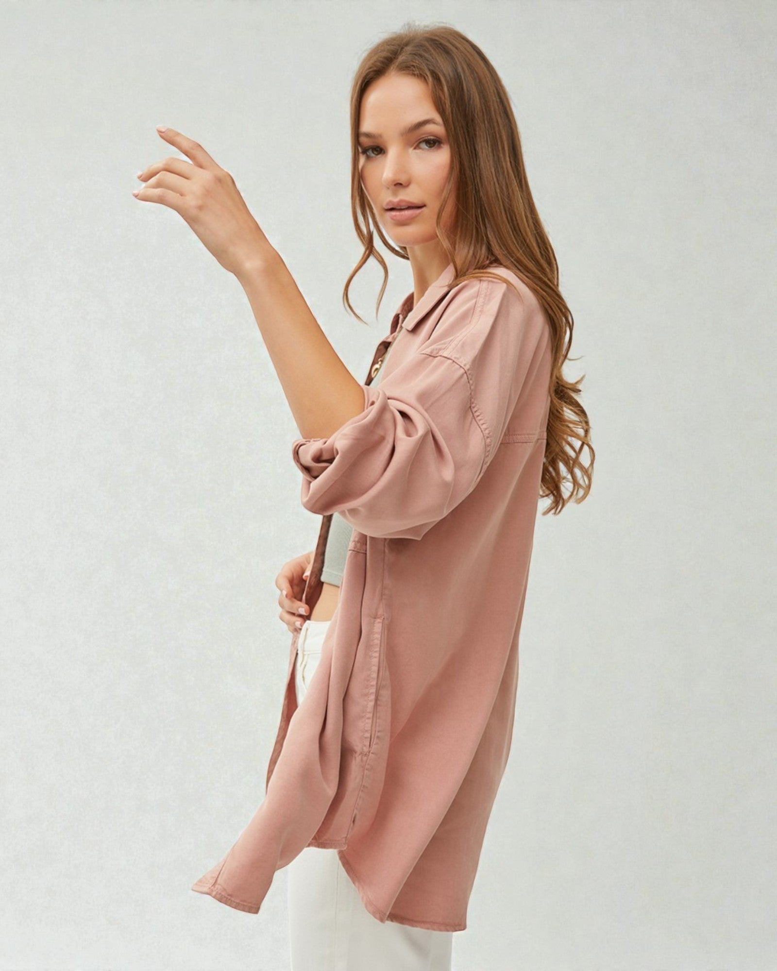 Woman wearing a long, light pink shirt against a plain background