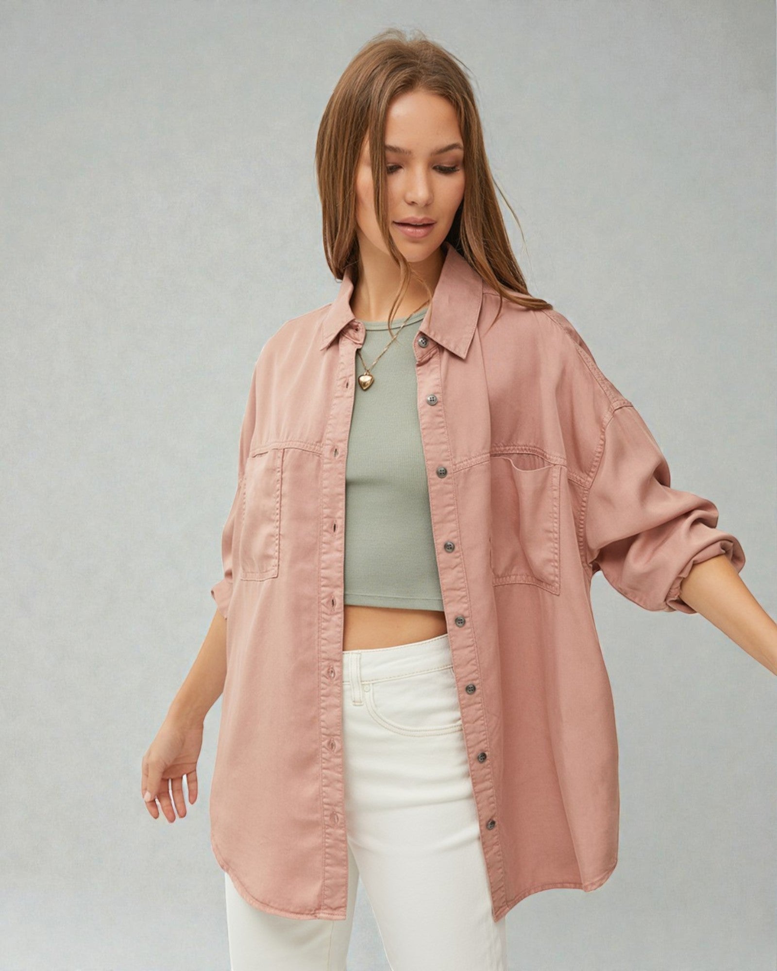 Woman wearing a pink jacket over a green top and white pants on a gray background