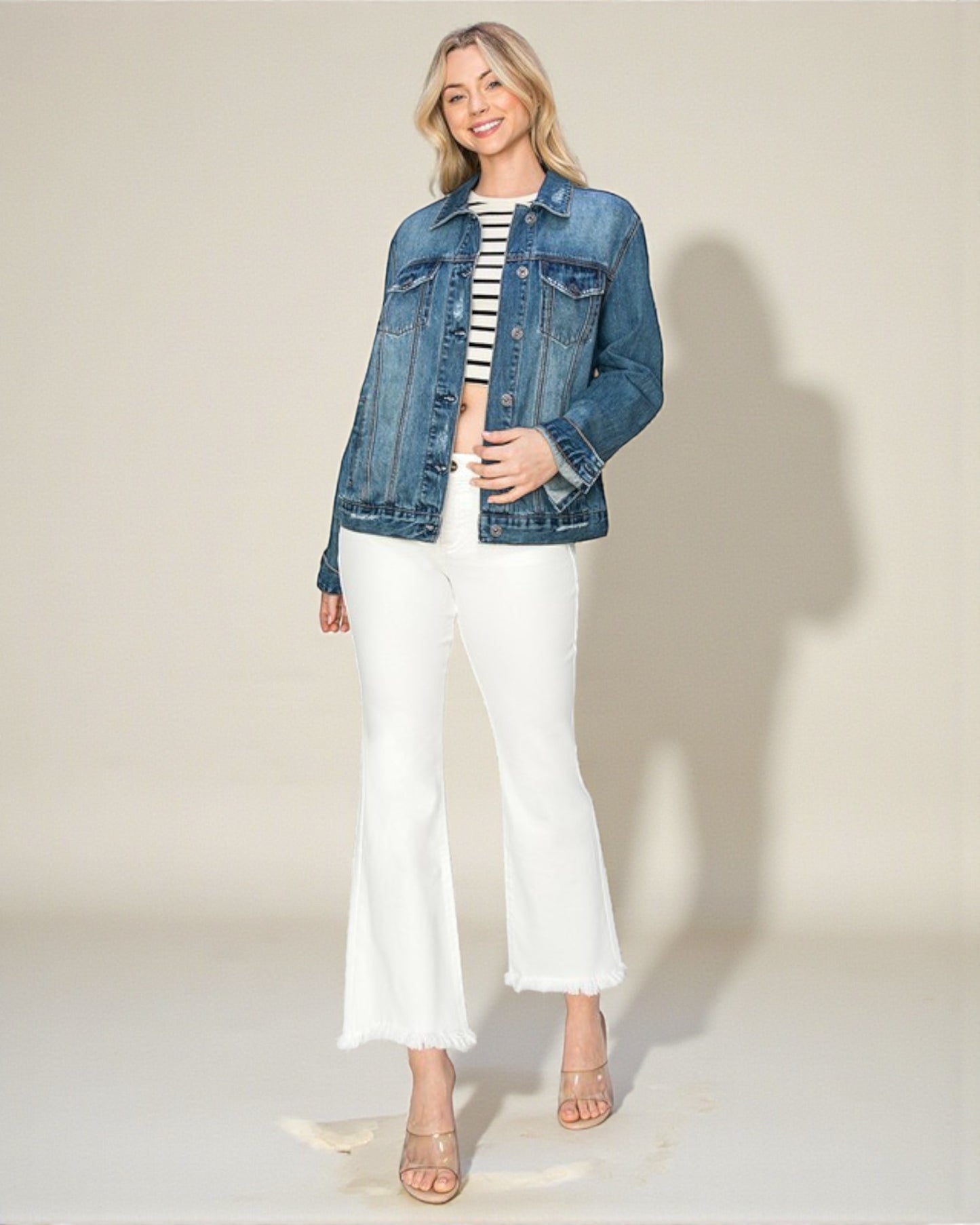 Woman wearing a denim jacket, striped top, and white pants on a plain background