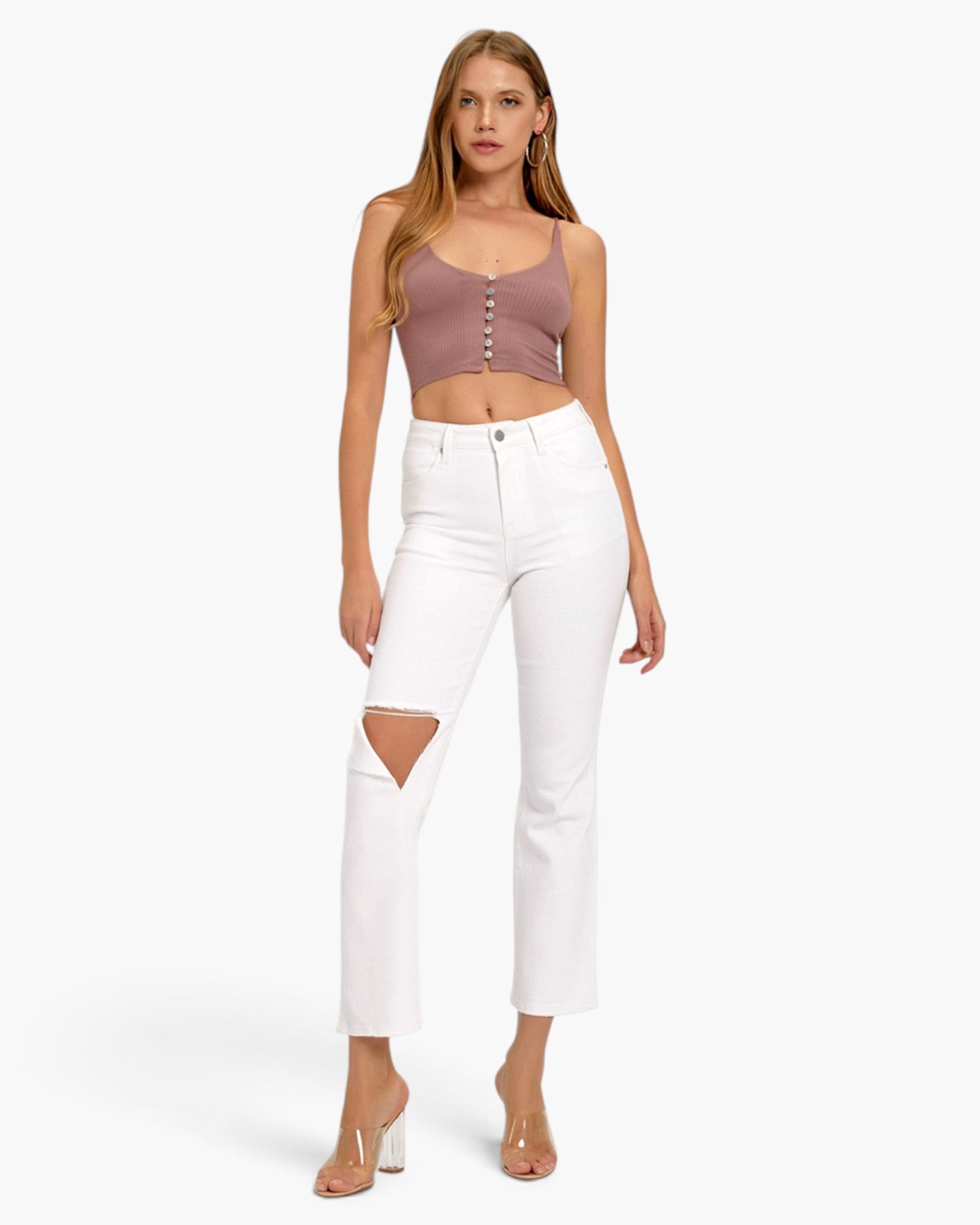A model wearing a dusty rose ribbed crop top with button details and white cropped jeans with a distressed knee cutout, paired with clear high-heeled sandals, against a light gray studio background.