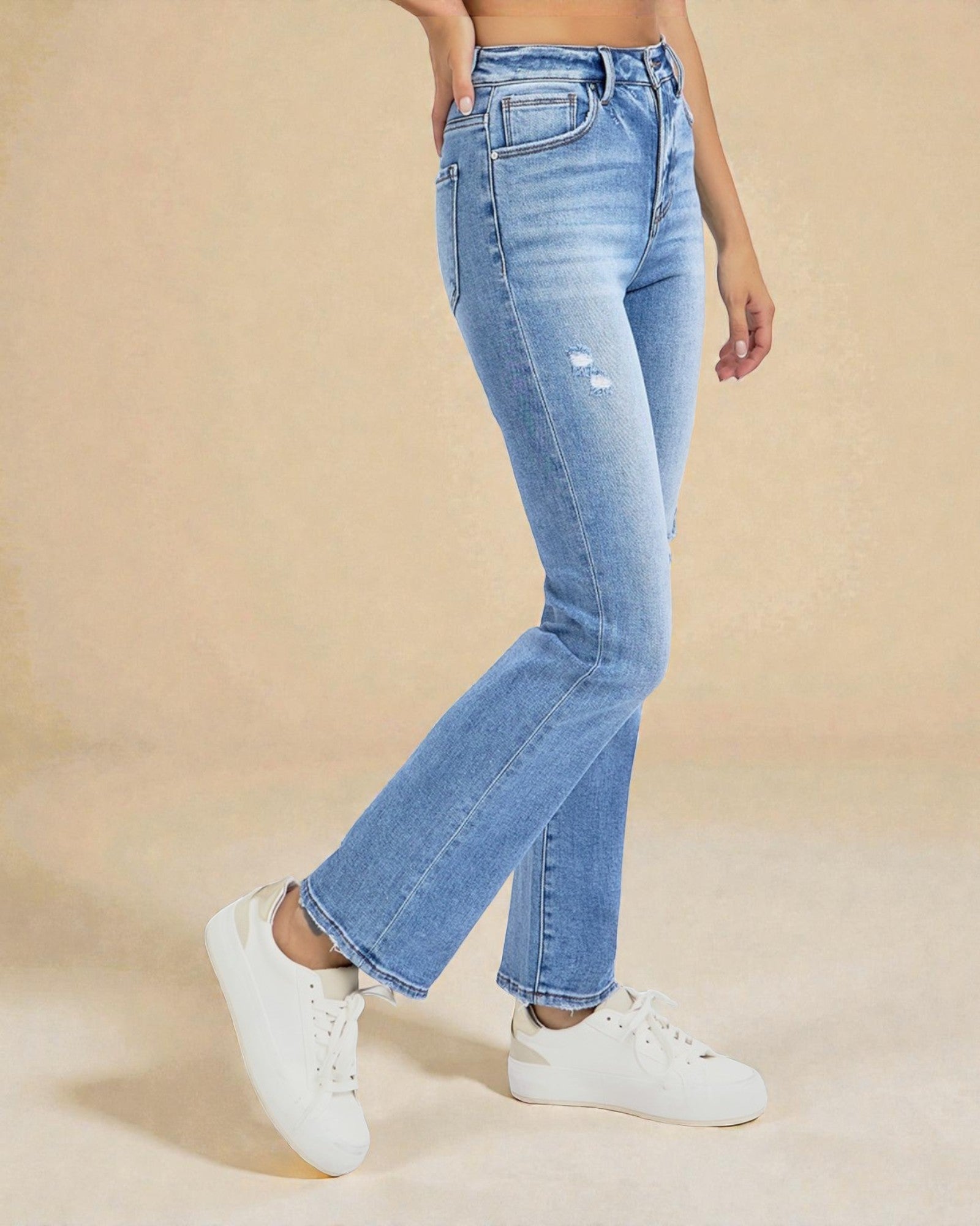Person wearing light blue jeans and white sneakers on a beige background