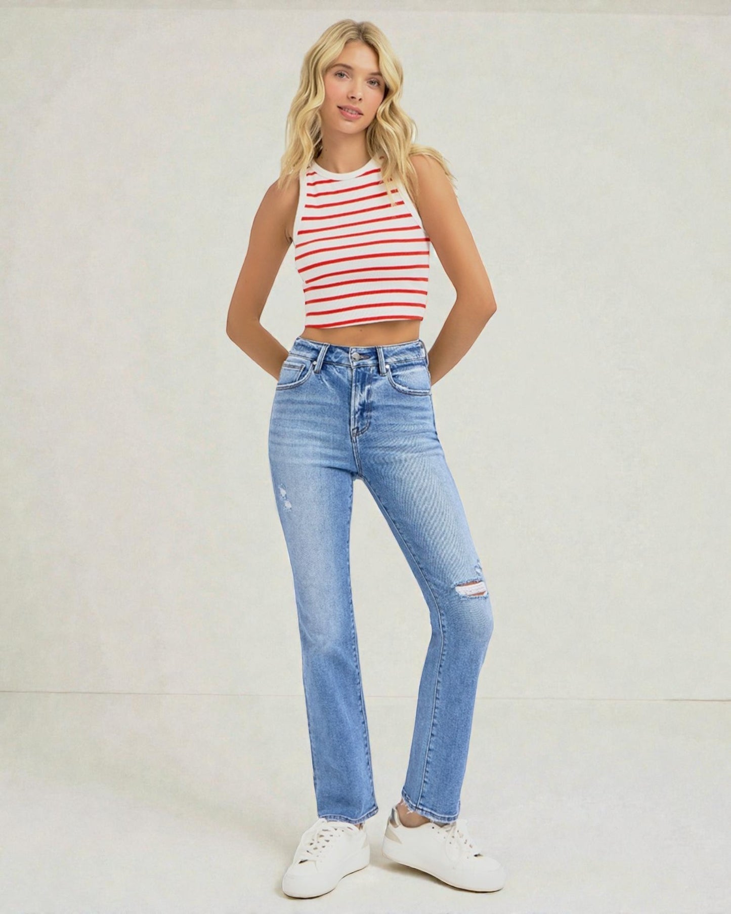 Woman wearing a red and white striped tank top and blue jeans on a plain background