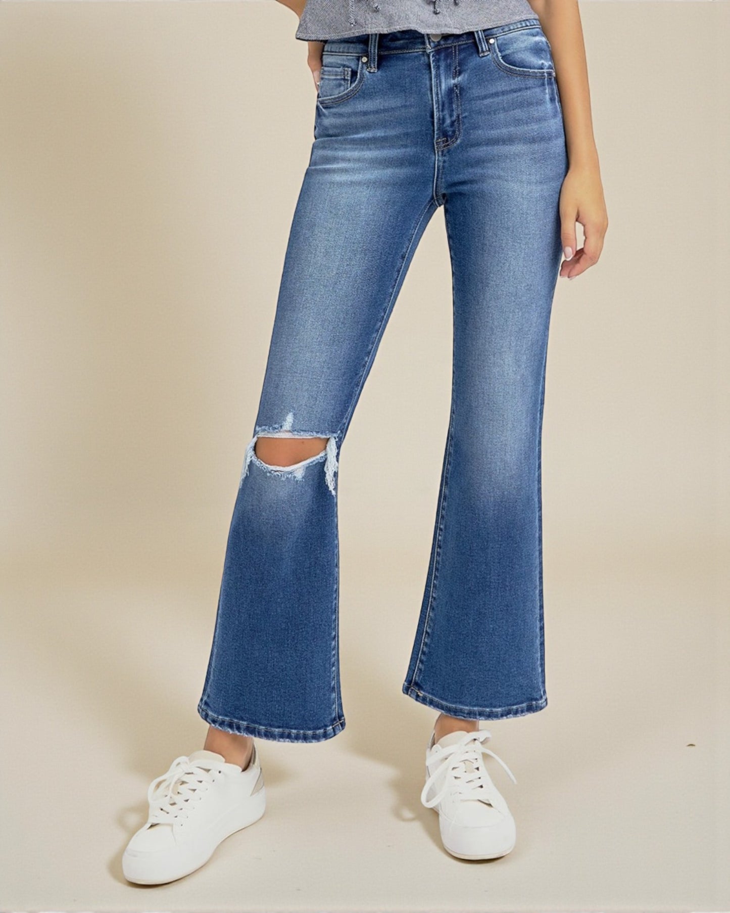 Person wearing blue flared jeans with a ripped knee on a beige background