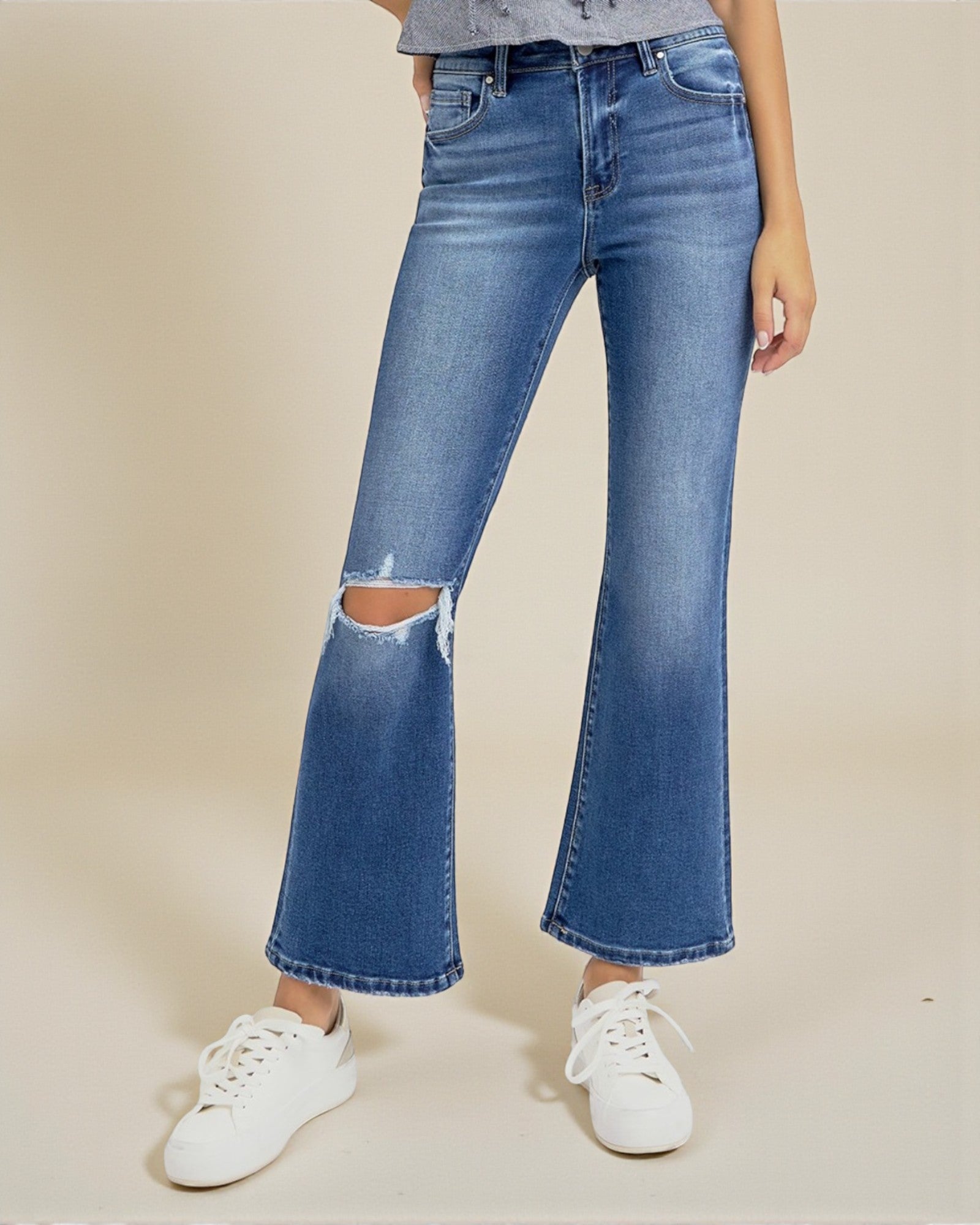 Person wearing blue flared jeans with a ripped knee on a beige background